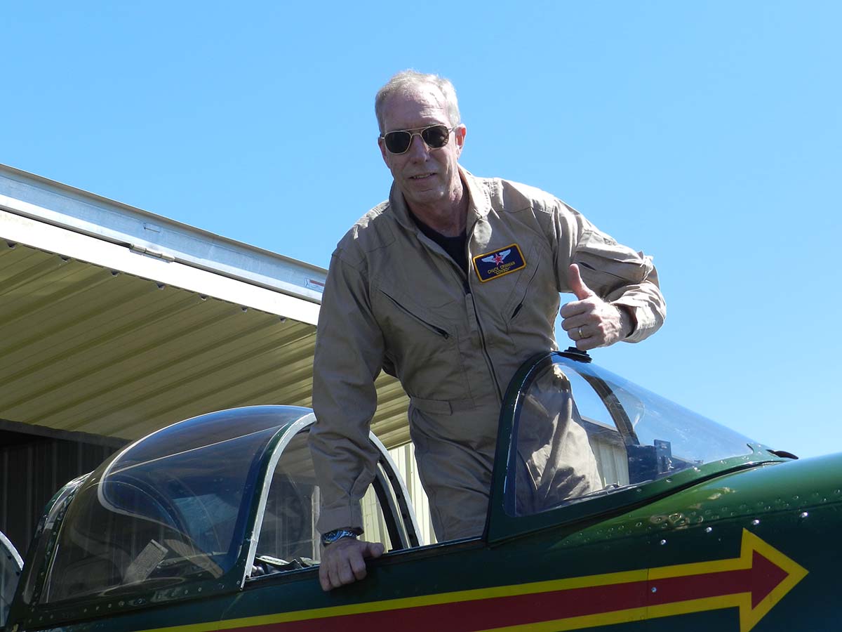 Chuck Crinnian stands in cockpit of plane and give thumbs up